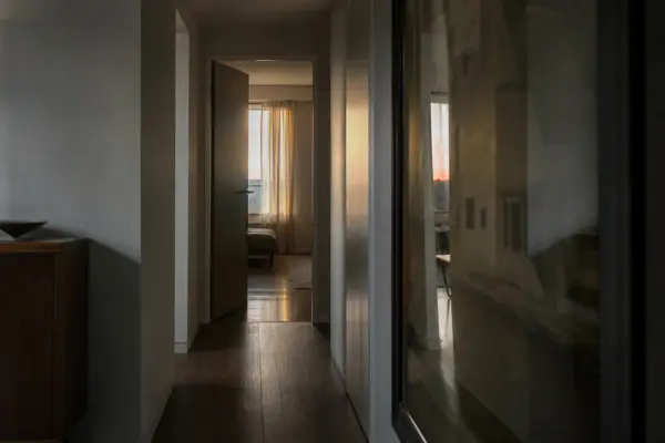 Corredor doméstico ao entardecer com porta entreaberta e reflexo do ambiente em um painel de vidro